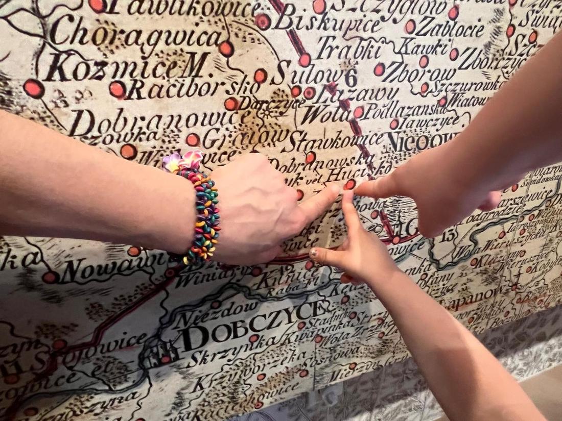 Dziecięce i dorosłe dłonie wskazują Dobczyce i okoliczne wsie na starej mapie